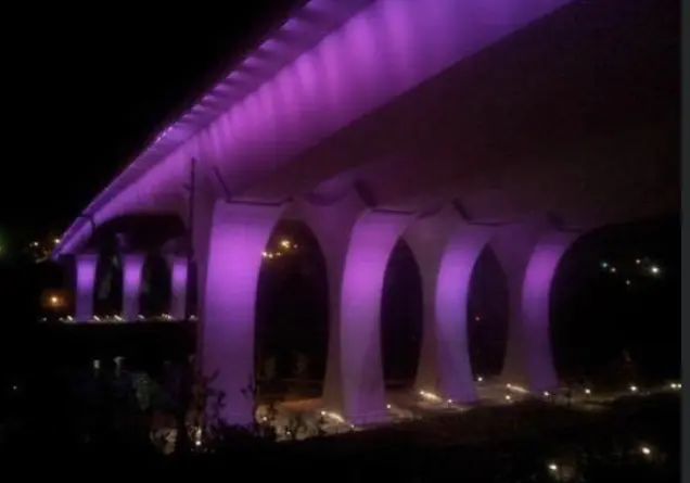 A purple light is on the side of a bridge.
