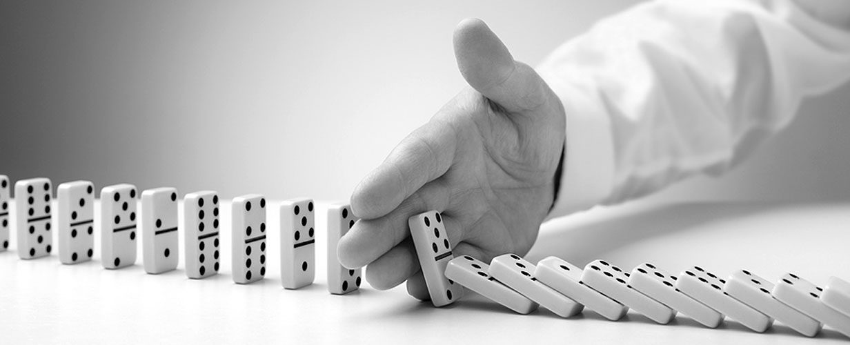 A hand is holding dominoes to stop the falling domino.